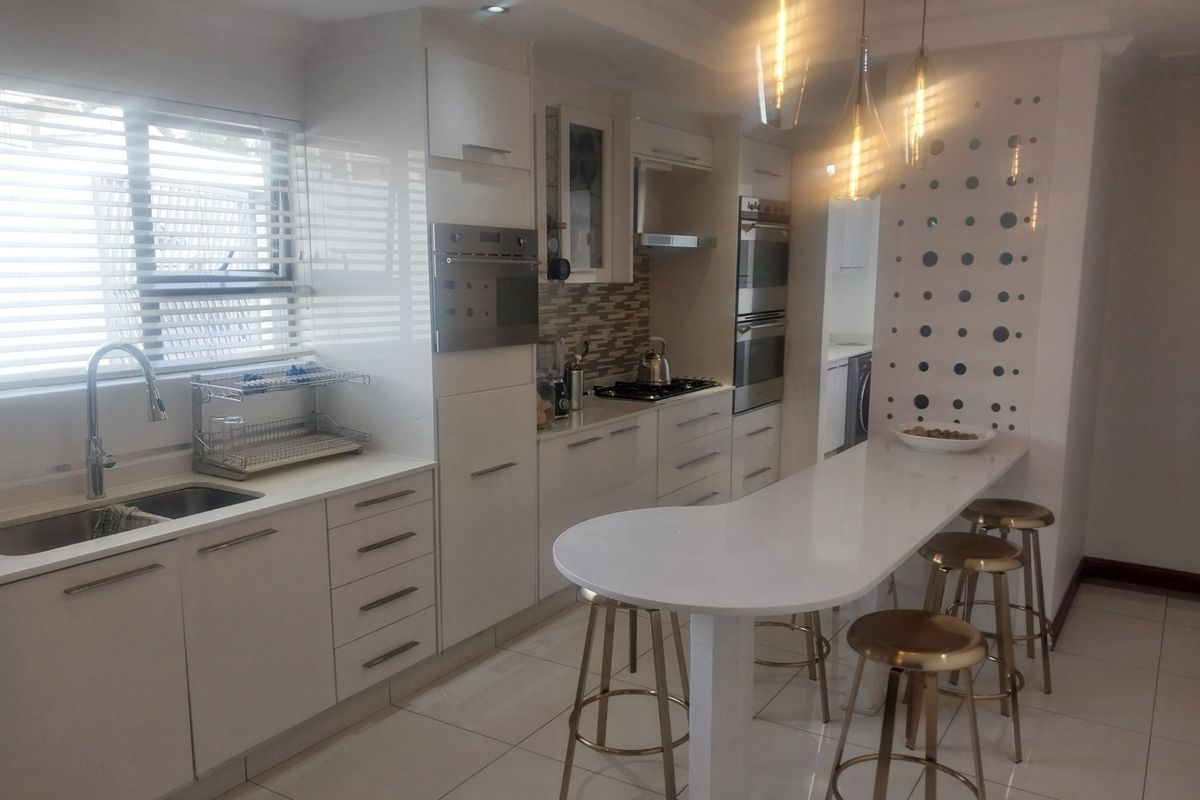 Modern kitchen featuring white cabinetry, stone countertops, built-in oven, gas hob, extractor fan, and a breakfast bar with pendant lighting.
