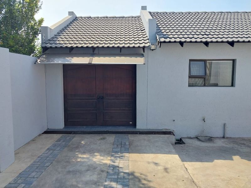 Exterior view of a garage featuring double wooden doors, a tiled roof, and a paved driveway area.