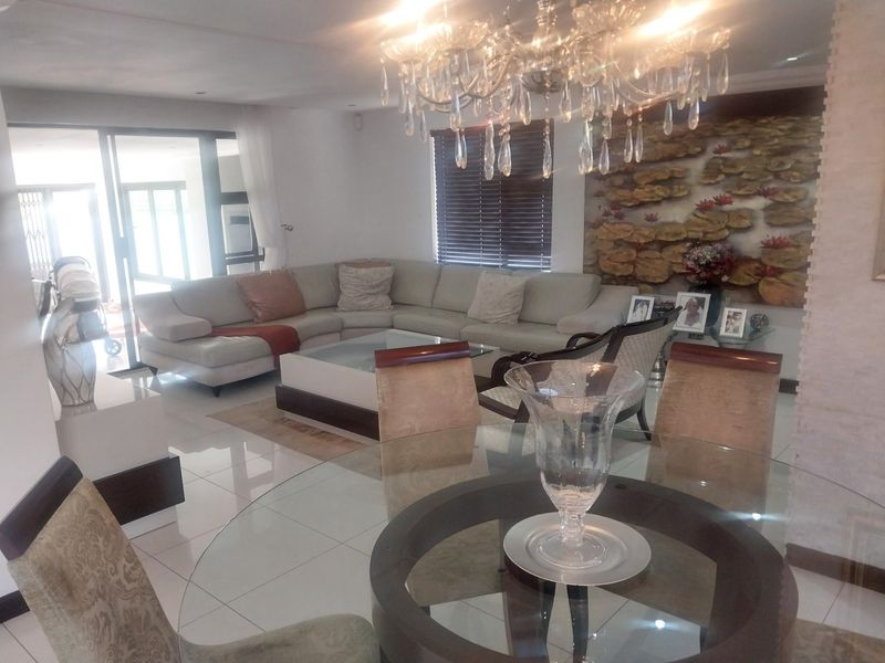 Spacious open-plan living and dining area featuring polished floor tiles, a decorative feature wall, and a large crystal chandelier.