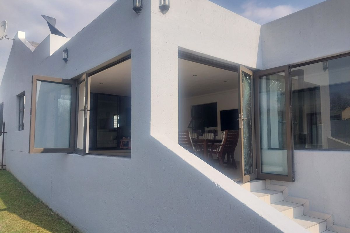 Exterior view of the rear facade featuring white rendered walls, aluminium framed doors, and tiled steps leading into the living area.