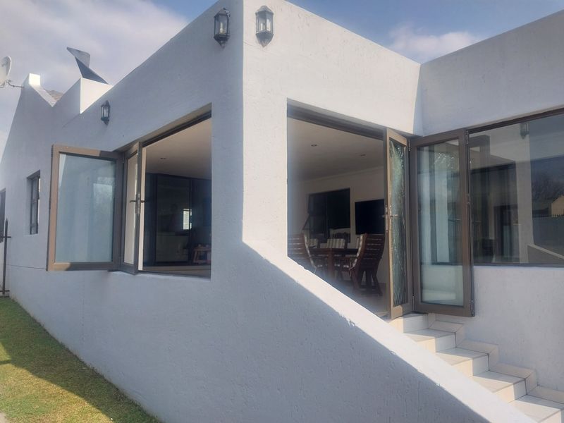 Exterior view of the rear facade featuring white rendered walls, aluminium framed doors, and tiled steps leading into the living area.