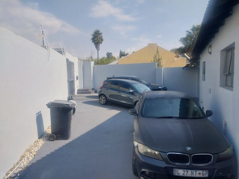 A paved driveway area leading to the side of the house, featuring high boundary walls with security fencing.