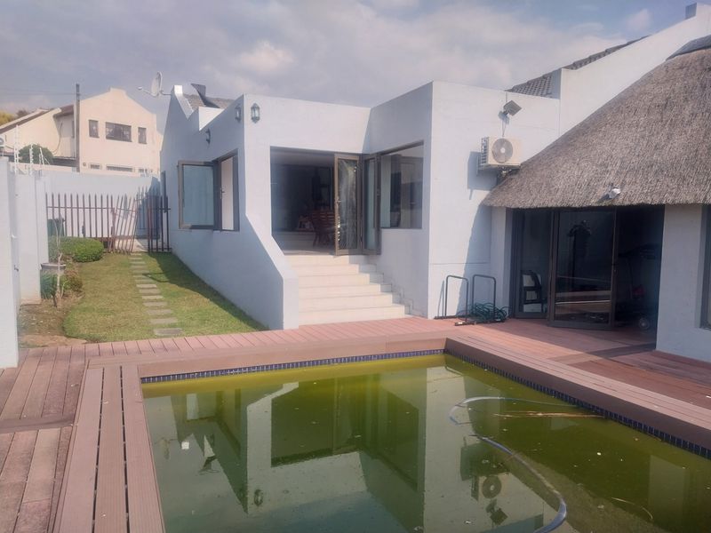 Rear exterior view featuring a swimming pool with timber decking, thatched roof section, and direct access to the living area via stairs.