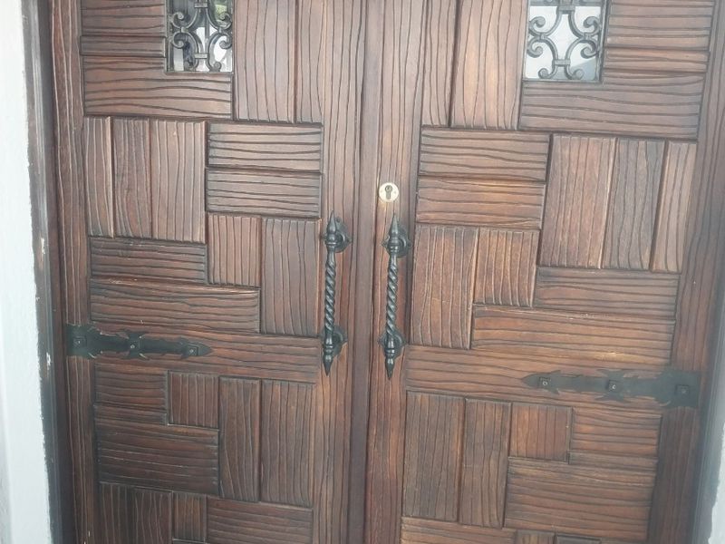 A solid timber double entrance door featuring decorative ironwork inserts and traditional wrought iron hardware.