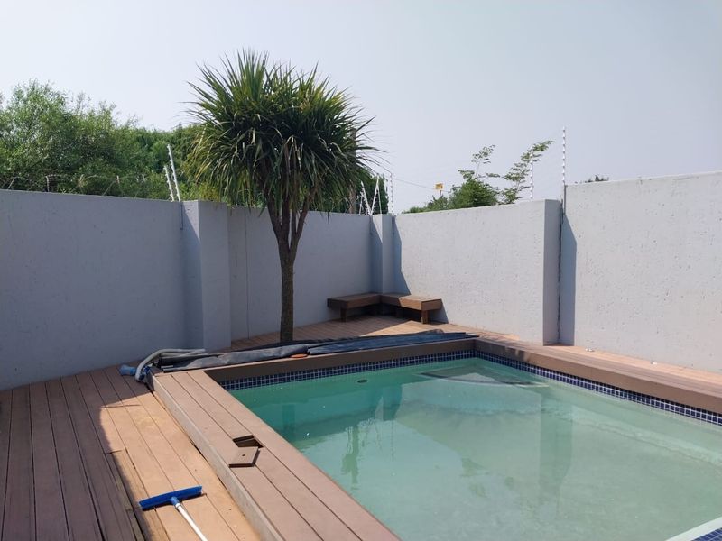A private pool area featuring a composite deck surround, perimeter boundary walls with electric fencing, and a built-in corner bench.