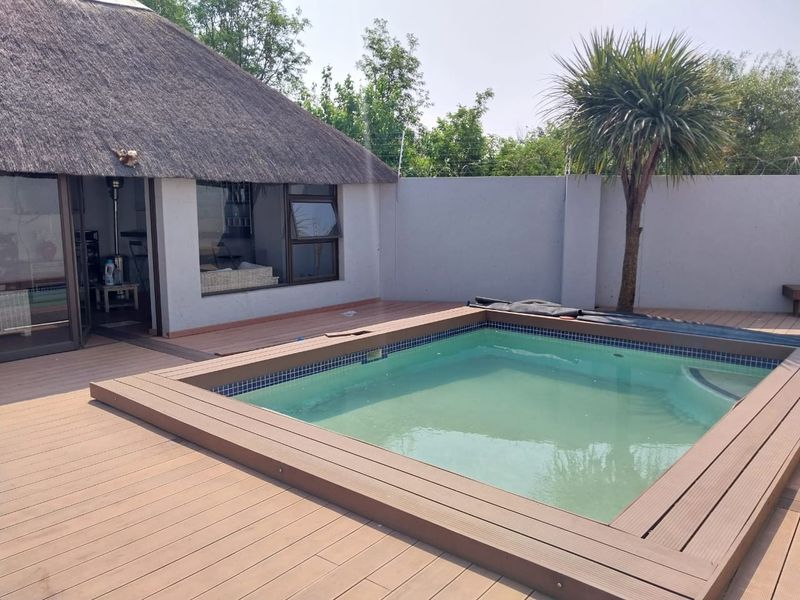 Outdoor pool area featuring a built-in swimming pool surrounded by composite decking, adjacent to a thatched-roof structure with sliding glass doors.