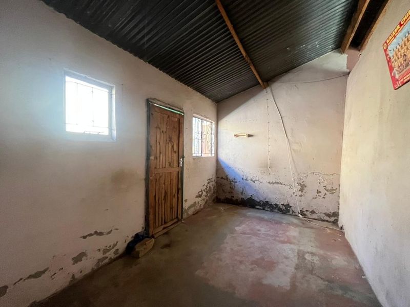 An empty room featuring a corrugated iron roof, timber door, and security-barred windows, requiring significant cosmetic renovation and wall repairs.