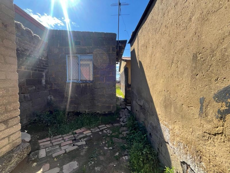 A narrow exterior side passage featuring exposed brick and plastered walls with a weathered brick pathway and visible signs of structural wear.