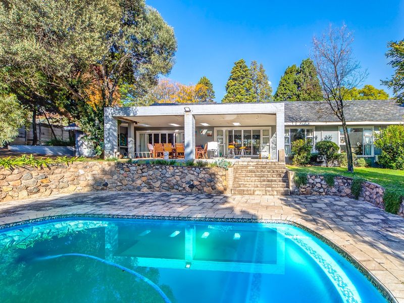 Spacious rear exterior featuring a swimming pool, stone retaining wall, and a covered patio area perfect for outdoor entertaining.