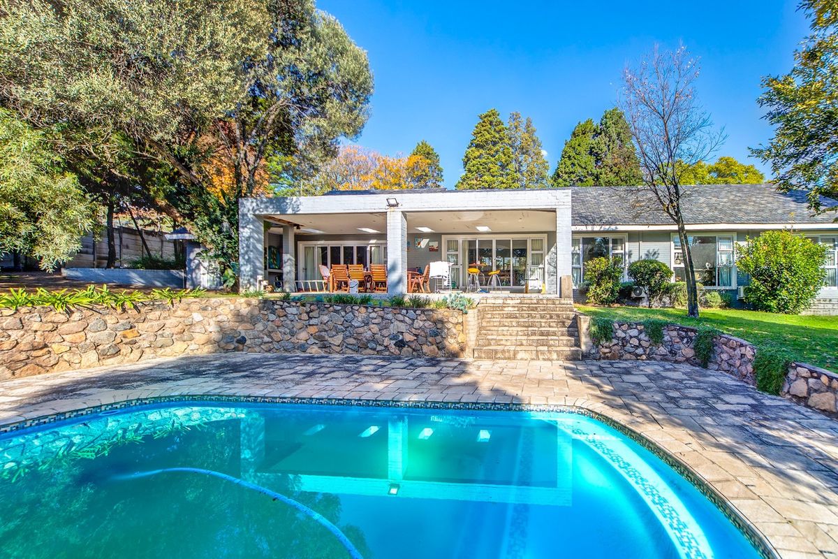 Spacious rear exterior featuring a swimming pool, stone retaining wall, and a covered patio area perfect for outdoor entertaining.