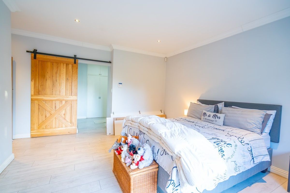 Spacious bedroom featuring light-toned wood-look flooring, recessed ceiling lighting, and a rustic sliding barn door leading to an adjacent area.