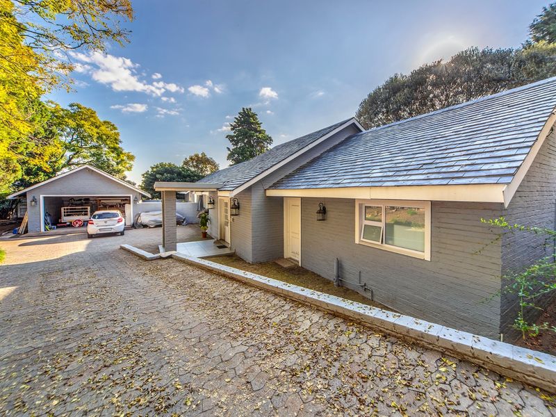 A well-maintained single-story residence featuring a painted brick exterior, pitched tiled roof, and a spacious paved driveway leading to a detached garage.