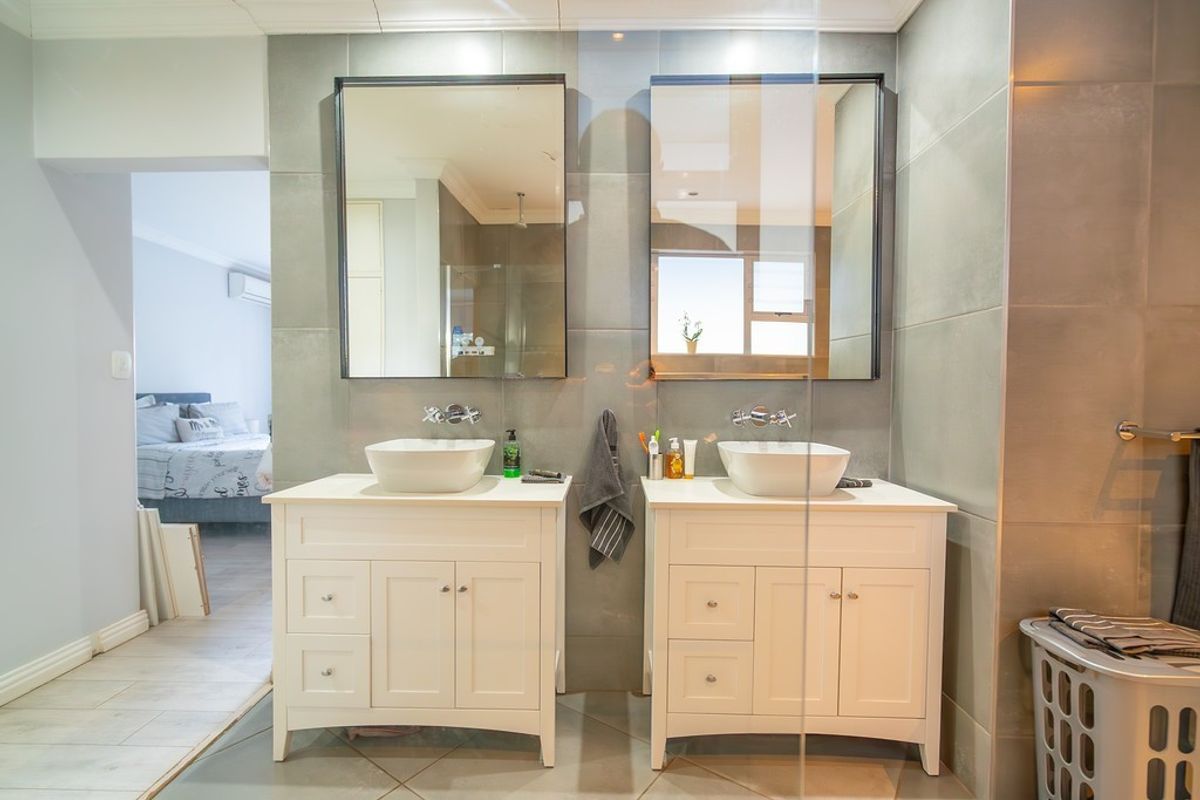 Modern bathroom featuring a double vanity with vessel sinks, wall-mounted faucets, and large framed mirrors against grey tiled walls.