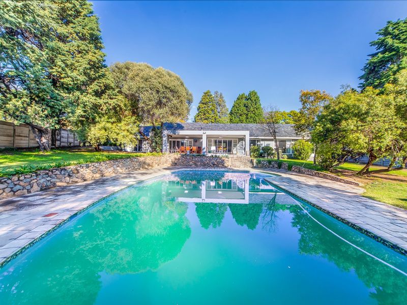 Spacious backyard featuring a large swimming pool, stone retaining wall, and a covered patio area overlooking the landscaped garden.