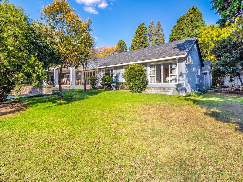 Spacious rear garden featuring a well-maintained lawn, mature trees, and a covered patio area attached to the main house structure.