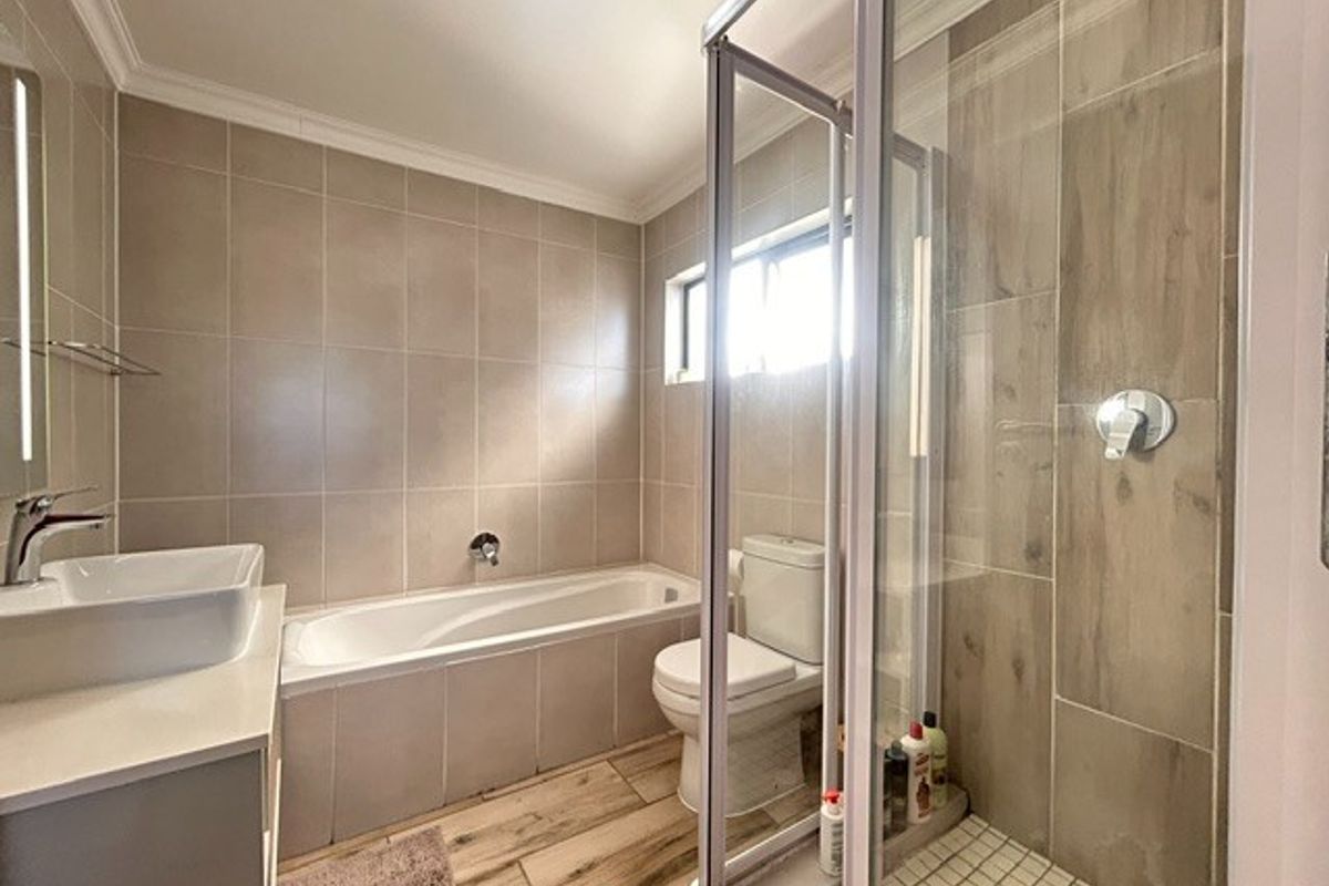 Modern bathroom featuring a tiled bathtub, separate glass-enclosed shower, and a contemporary vanity basin with neutral wall and floor tiling.