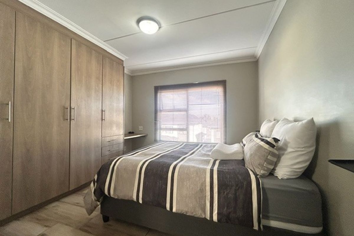 A well-maintained bedroom featuring built-in wooden cabinetry, tiled flooring, and a built-in desk area under the window.