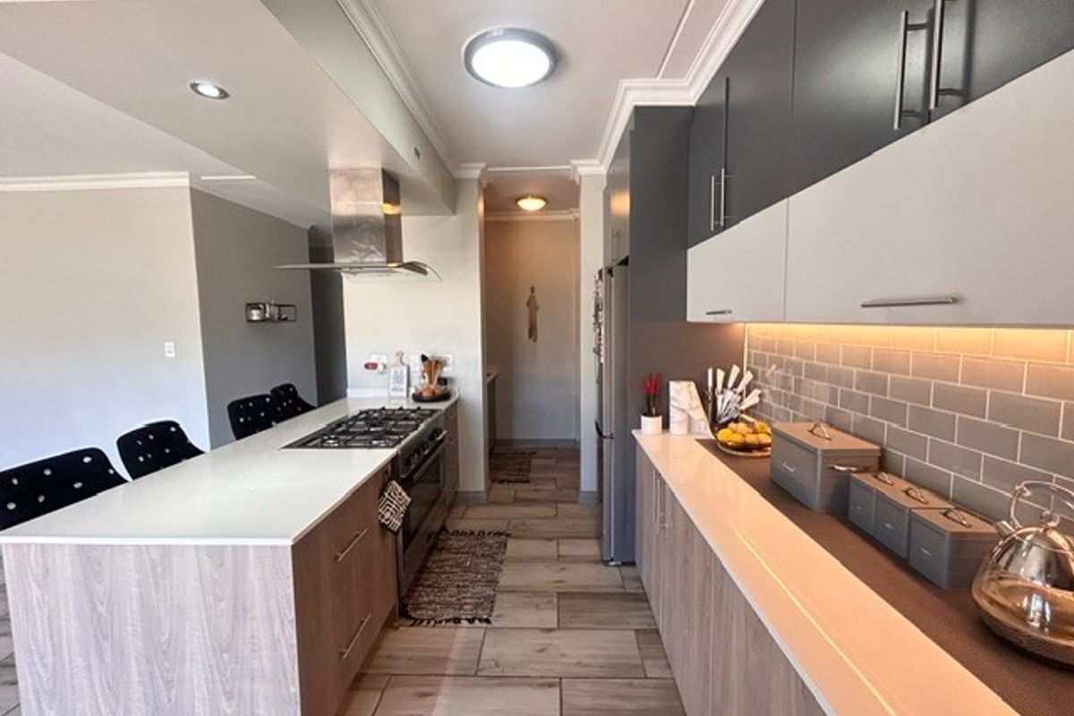 Modern kitchen featuring a central island with a built-in gas hob, extractor fan, stone countertops, and contemporary two-tone cabinetry with under-cabinet lighting.
