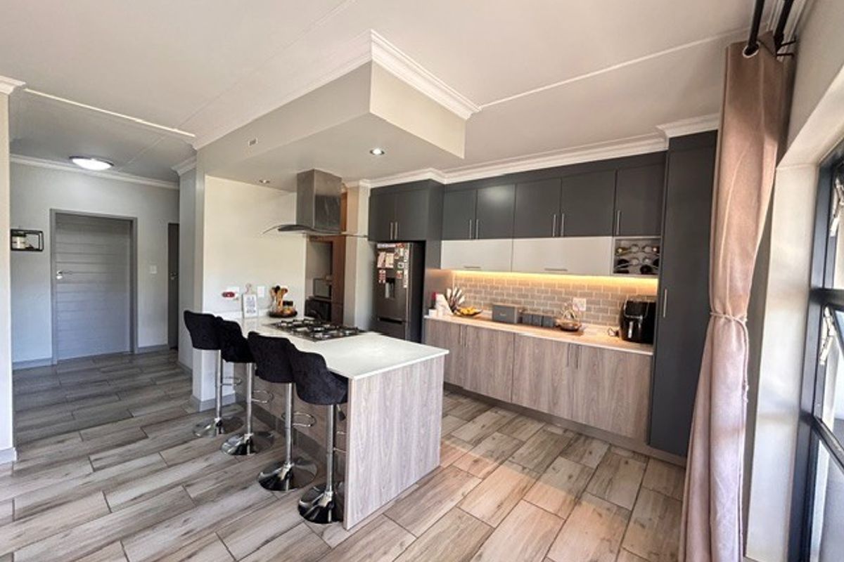 Modern kitchen featuring a central island with gas hob, sleek two-tone cabinetry, under-cabinet lighting, and durable wood-look floor tiles.