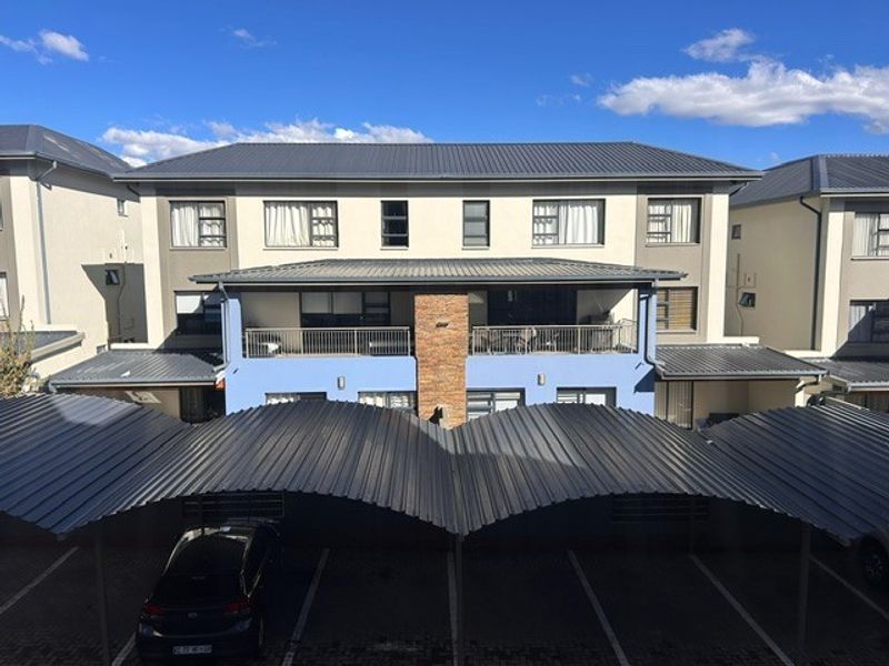 Front elevation of a multi-story townhouse complex featuring covered parking bays, a central brick pillar, and upper-level balconies.