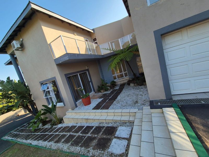 Front exterior view of a two-story house featuring a paved entrance, balcony with glass balustrade, and an integrated garage.