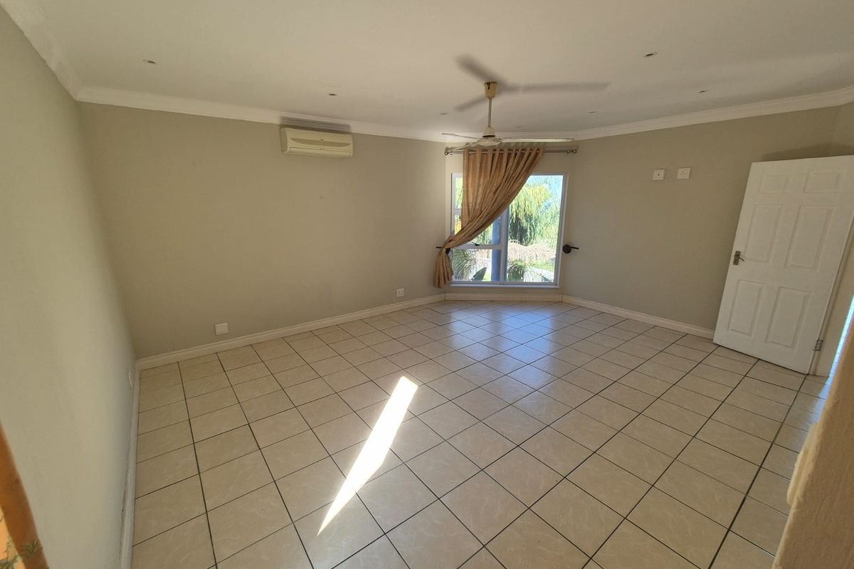 A spacious, empty bedroom featuring neutral tiled flooring, a ceiling fan, and a wall-mounted air conditioning unit.