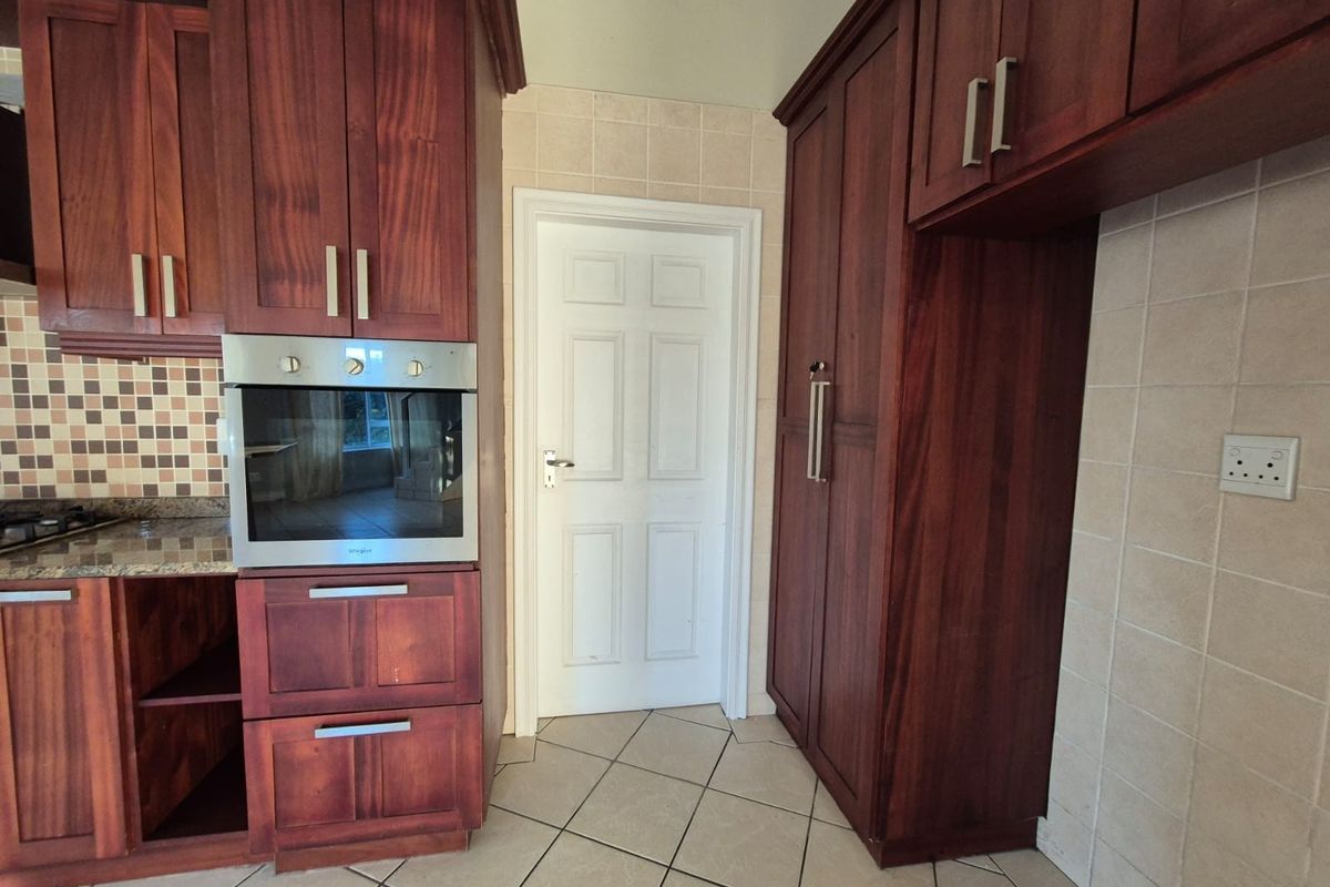 A kitchen area featuring dark wood cabinetry, built-in oven, granite countertops, and tiled flooring with a neutral backsplash.