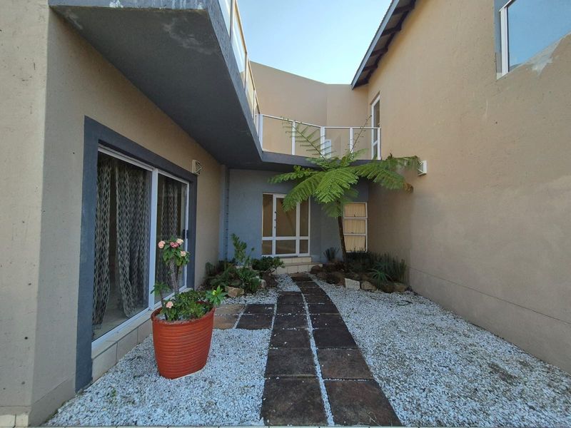 A private courtyard area featuring a paved walkway, gravel landscaping, and a balcony overlooking the ground level entrance.