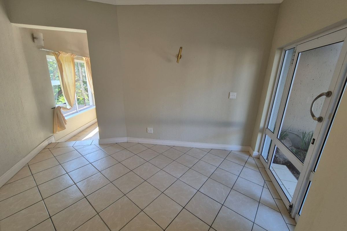 A bright, empty living area featuring neutral ceramic floor tiles, coved cornicing, and a glass-paneled door leading to an outdoor space.