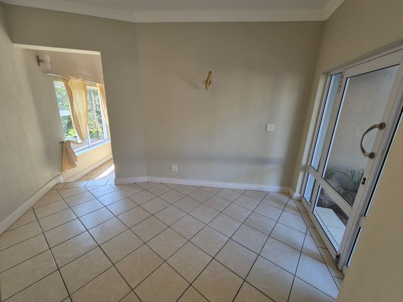 A bright, empty living area featuring neutral ceramic floor tiles, coved cornicing, and a glass-paneled door leading to an outdoor space.