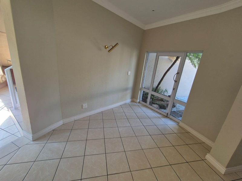 A bright entrance hall featuring neutral tiled flooring, crown molding, and a glass-paneled door providing natural light and garden views.