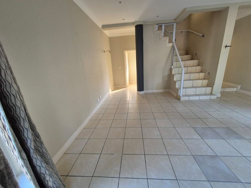 An open-plan living area featuring tiled flooring, a central structural column, and a staircase with a white metal railing leading to the upper level.