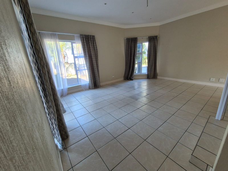 Spacious, light-filled living area featuring neutral ceramic floor tiles, large windows with curtain tracks, and recessed ceiling lighting.