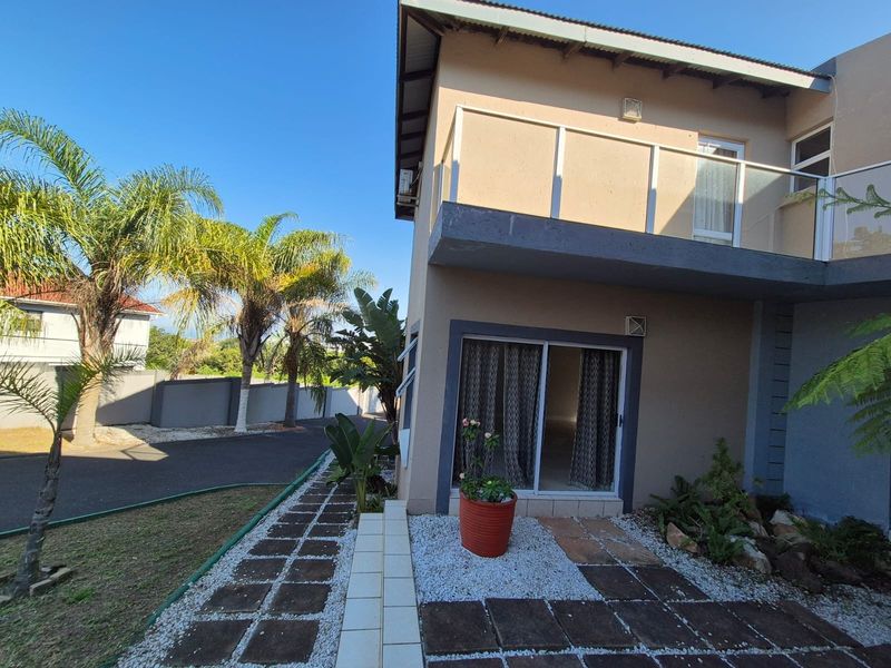 A two-story residential exterior featuring a ground-level patio with sliding glass doors and an upper-level balcony with glass balustrades.