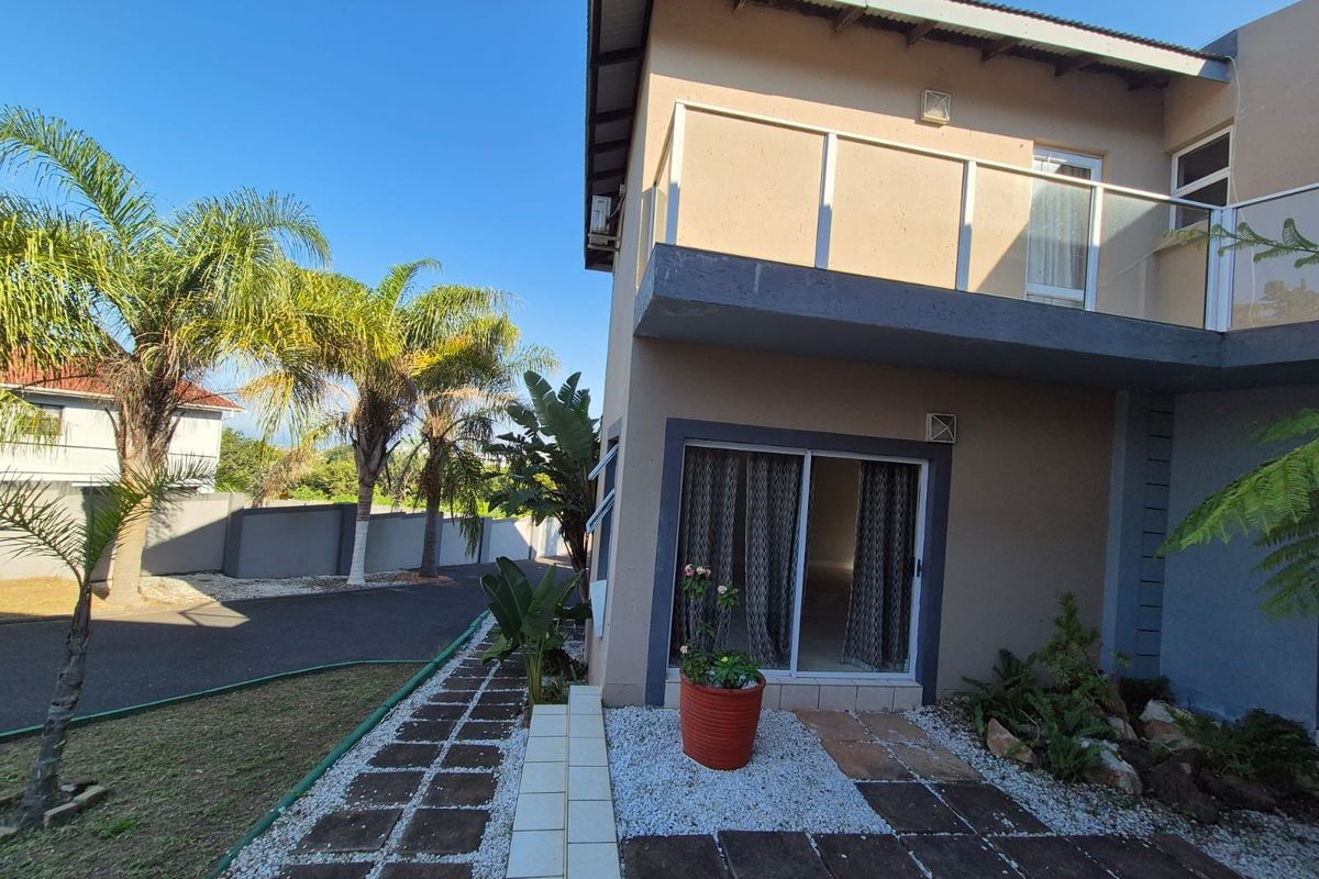 A two-story residential exterior featuring a ground-level patio with sliding glass doors and an upper-level balcony with glass balustrades.