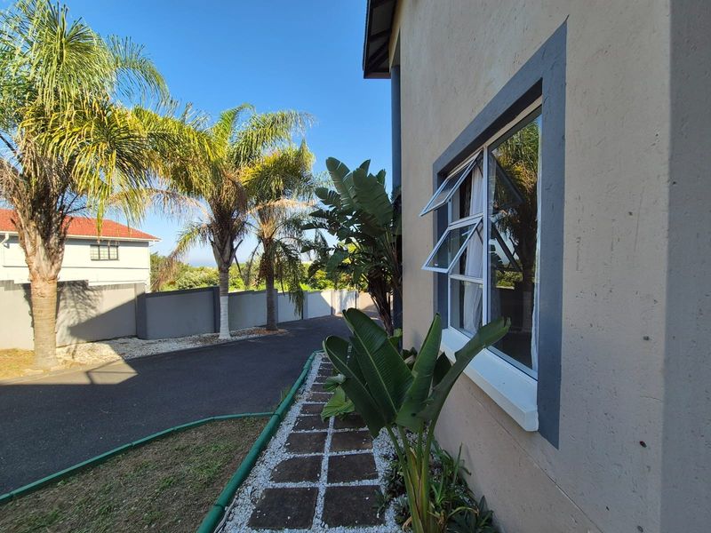 Side exterior view of the property featuring a paved walkway, landscaped garden beds, and a window with a dark frame.