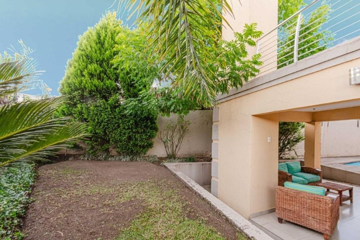 A private rear garden area featuring a covered patio space, tiled flooring, and a small lawn area adjacent to the townhouse structure.