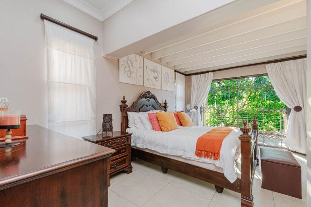 A well-lit bedroom featuring tiled flooring, crown molding, and a large sliding door with security gate leading to an outdoor area.