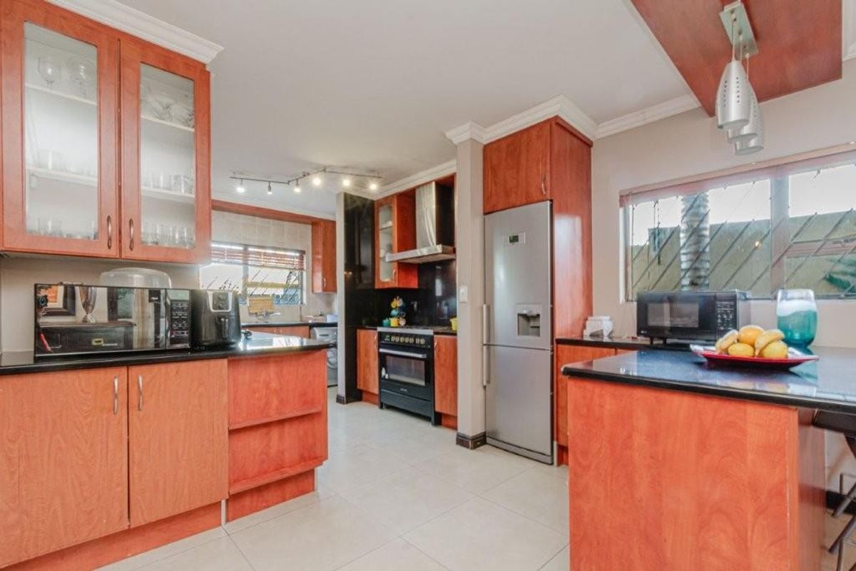 A functional kitchen featuring wood-finish cabinetry, dark countertops, a built-in oven with extractor fan, and tiled flooring.