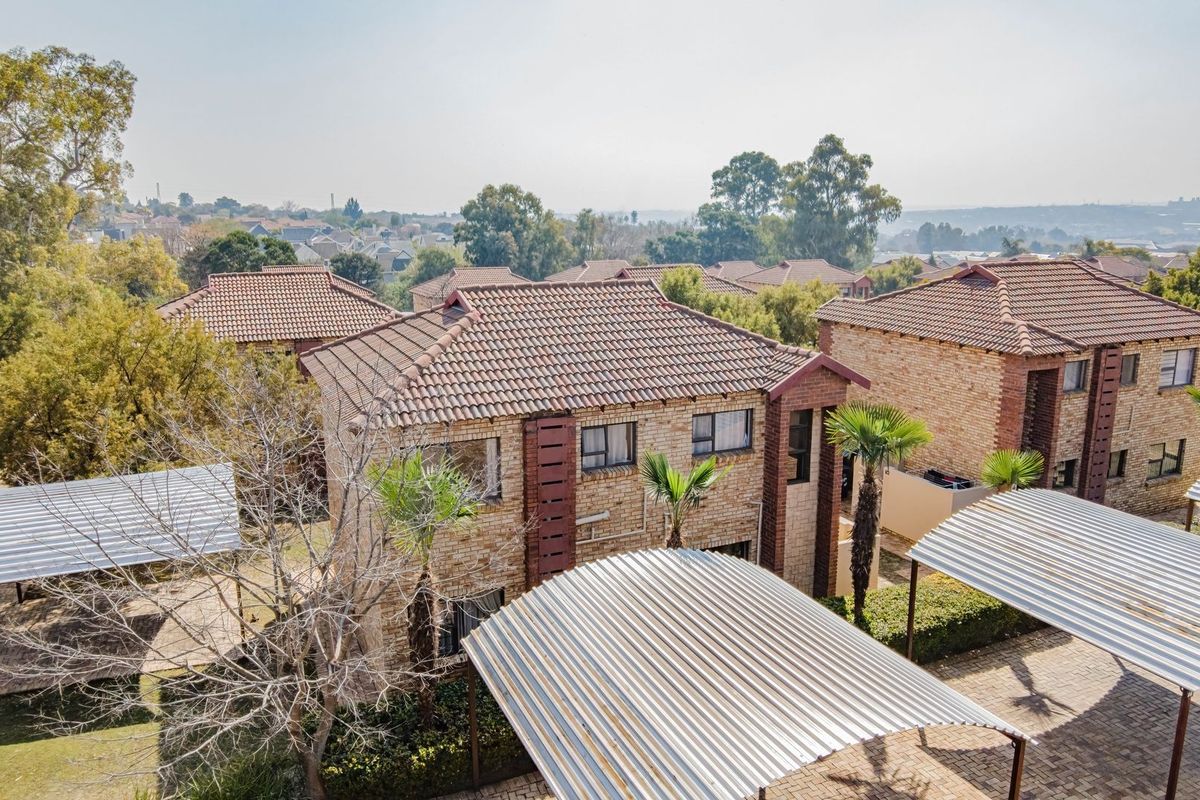 Aerial view of a residential apartment complex featuring face-brick buildings, tiled roofs, and covered carport parking areas within a landscaped estate setting.