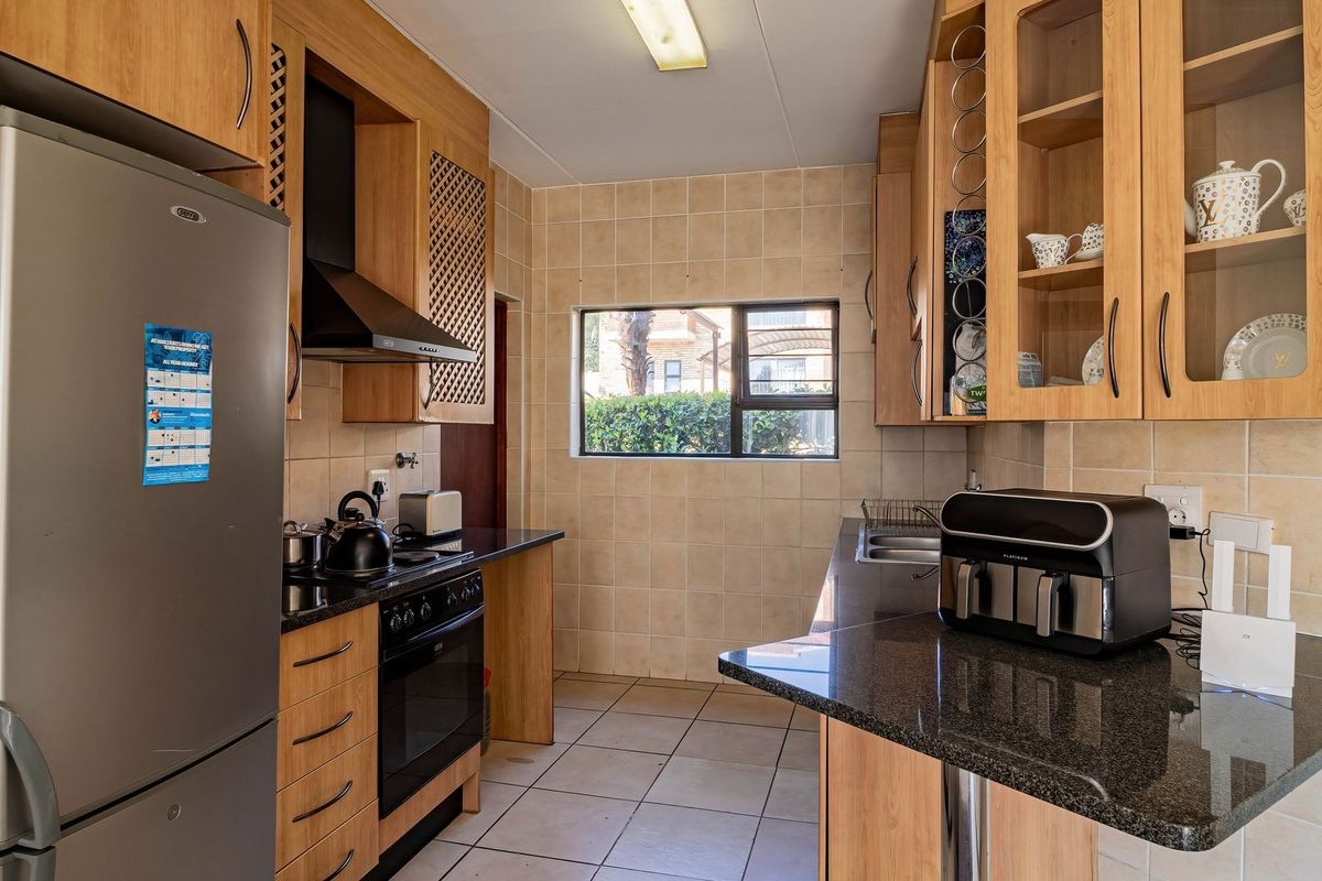 A functional kitchen featuring light wood cabinetry, dark granite countertops, a built-in oven with extractor fan, and tiled finishes throughout.