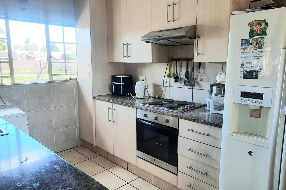 Functional kitchen featuring light-toned cabinetry, granite-look countertops, built-in oven, electric hob, and stainless steel extractor fan with tiled flooring.