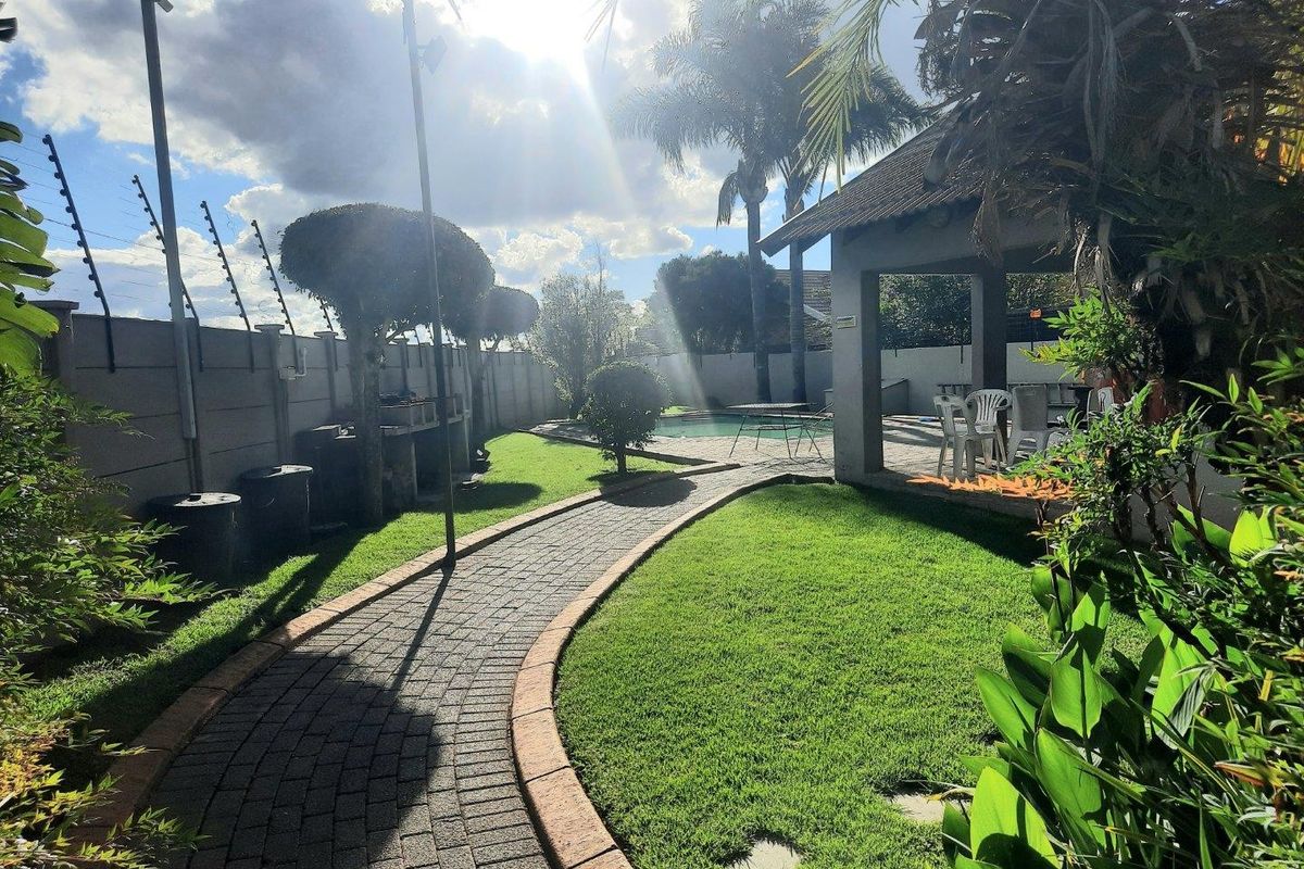 A well-maintained outdoor area featuring a paved walkway, lush lawn, swimming pool, and a covered patio structure.