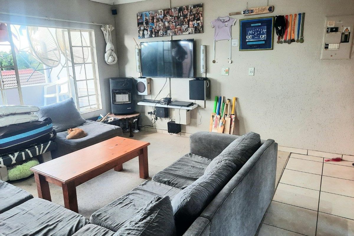 A living room featuring tiled flooring, large windows providing natural light, and a wall-mounted television setup.