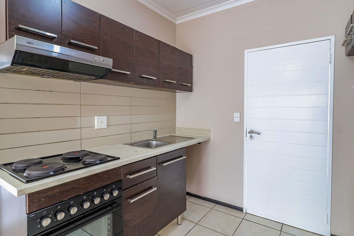 A functional kitchen featuring dark wood-finish cabinetry, a built-in stove with extractor fan, tiled backsplash, and tiled flooring.