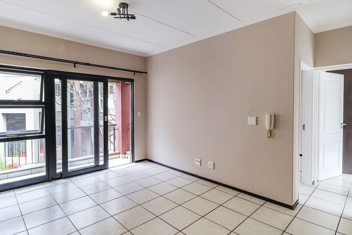 An empty living room featuring tiled flooring, a sliding glass door leading to a balcony, and a wall-mounted intercom system.