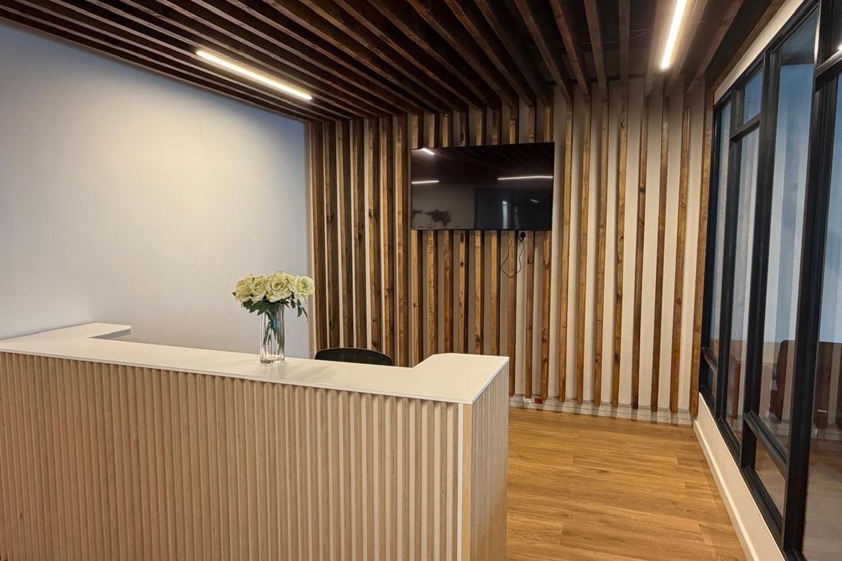 Modern office reception area featuring a custom slatted wood feature wall, integrated linear lighting, and a sleek built-in reception desk.