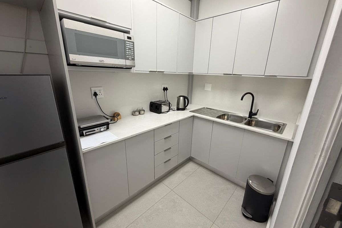 A compact, modern office kitchenette featuring light grey cabinetry, stone-look countertops, a stainless steel double sink, and a built-in microwave.