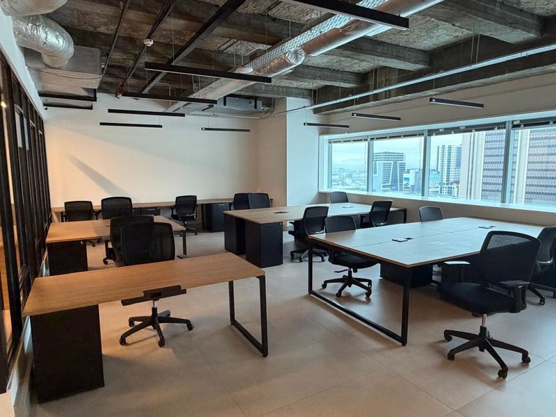 Modern open-plan office space featuring an industrial-style exposed concrete ceiling, large windows with city views, and tiled flooring.
