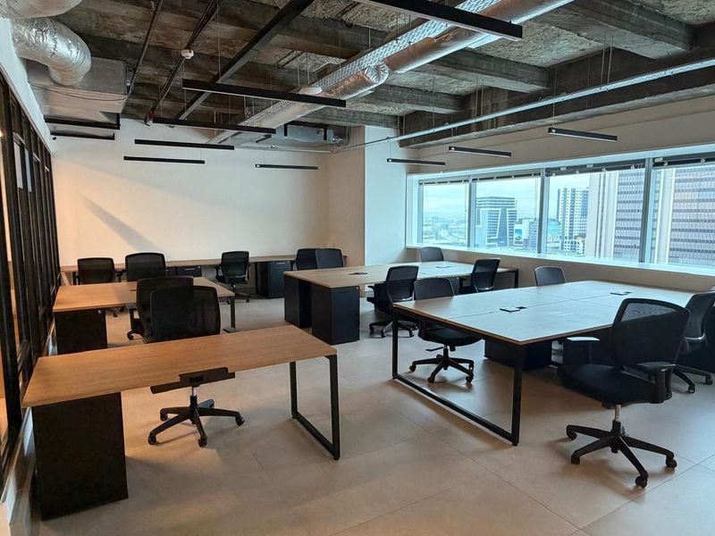 Modern open-plan office space featuring an industrial-style exposed concrete ceiling, large windows with city views, and tiled flooring.